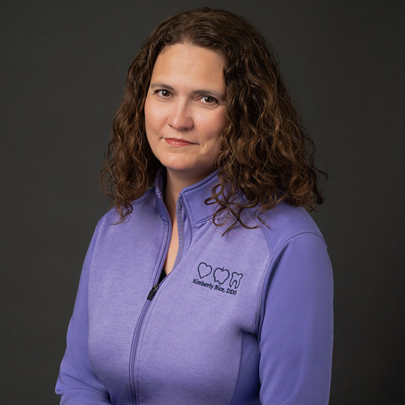 Amy, our Office Manager wearing a sweater with the corporate logo and smiling