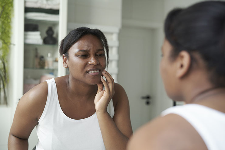 Woman looking in the mirror holds her had to her jaw and grimaces